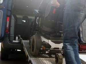 A bloke helps with wheelchair transportation problems using a ramp into a van.