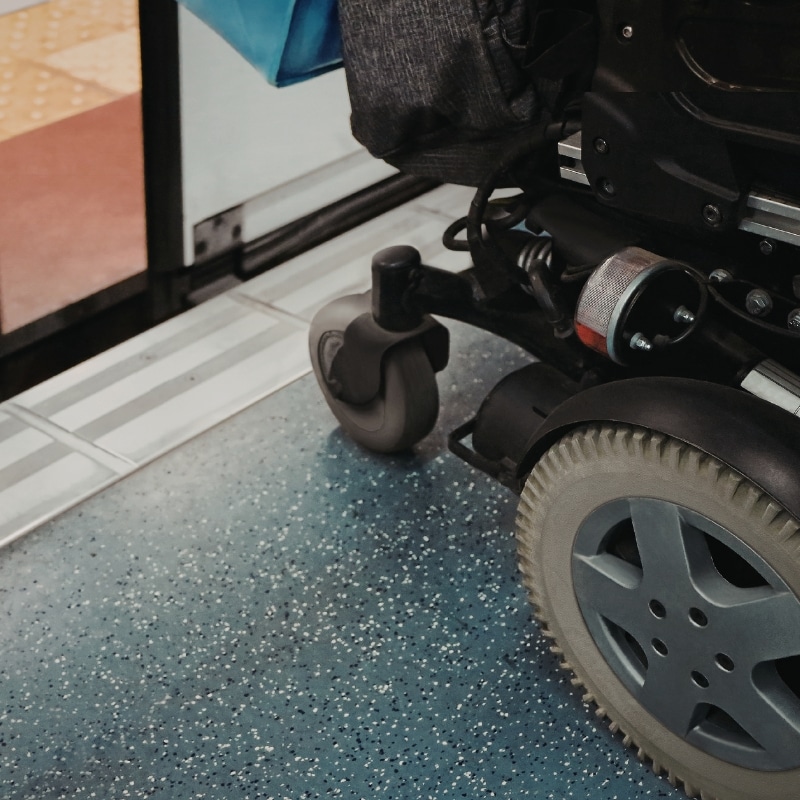 Assist with travel transport showing a powered wheelchair entering a vehicle via an accessible ramp with non-slip flooring.